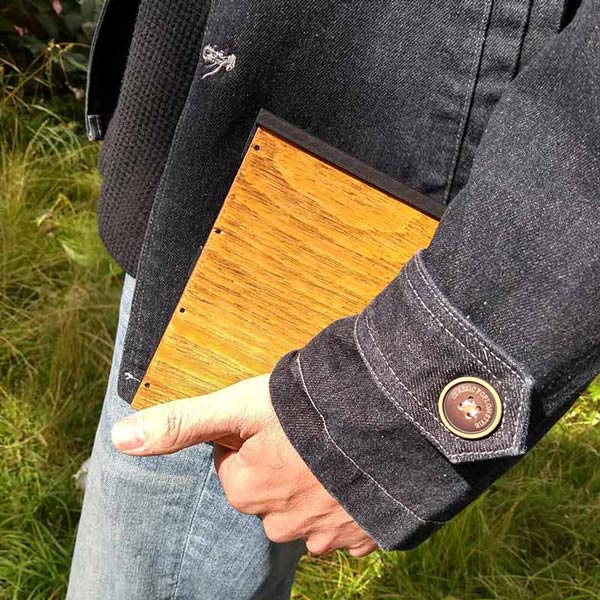 A close up of a hand carrying a beautiful brown wooden box for plein air painting