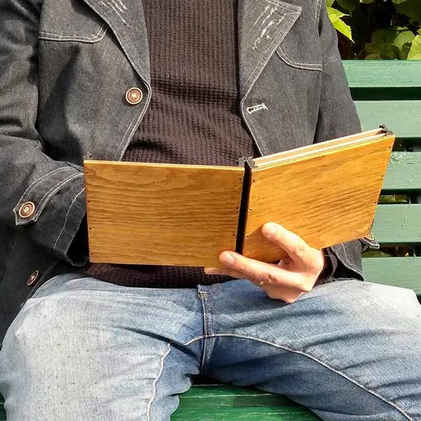 A person sitting in the nature and holding the pochade box with one hand like a open book and use the box to paint plein air art